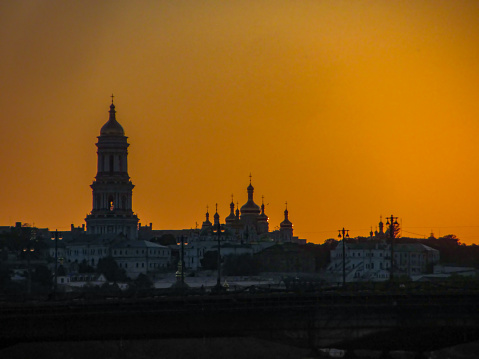 Golden dawn at Kyiv. View of the Kiev-Pechersk Lavra and the left bank. Silhouette panorama at sunset of the colorful sky over the Dnieper river with passing ducks in Kyiv