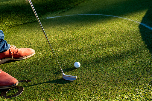 photo of man in brown shoes is playing golf on lawn