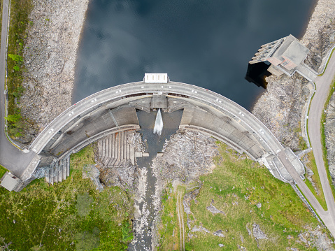 Aerial drone view of a hydro electric dam, in a remote location of the Scottish Highlands. It shows water being released from a reservoir where electricity is generated. Water levels are lower than normal, due to climate change, less rainfall and warmer weather than in previous years.