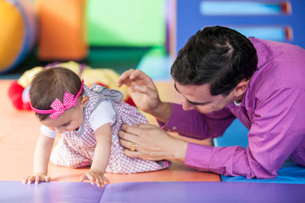赤ん坊の娘と遊ぶ若い父親。幼児のための早期刺激のコンセプト。 - physical therapy ストックフォトと画像