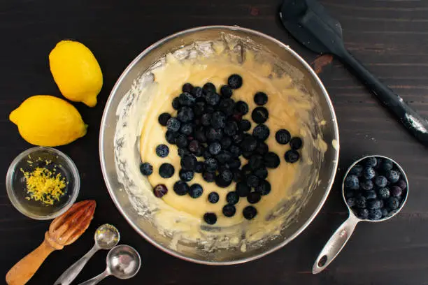 Bowl of blueberry muffin batter surrounded by fresh ingredients and kitchen utensils