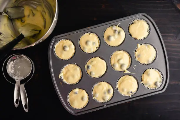 Unbaked blueberry muffin batter in a muffin pan with kitchen tools