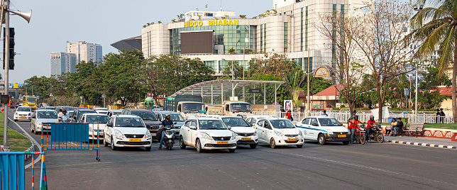 Kolkata, India - 29th March 2023: Vehicles stopped at traffic lights on Major Arterial Road in the Biswa Bangla  Gate area of New Town, Kolkata, India. The headquarters building (Bhaban) of HIDCO, the West Bengal Housing Infrastructure Development Corporation is in the background.