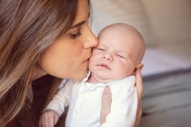 Mother holding her little blond son, kissing each other and enjoying time together at home