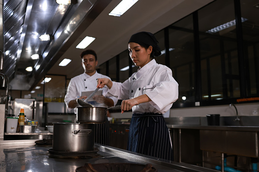Female  Chef teaching the student how to cook soup,  A female Chef in the kitchen provides cooking training to her students. Male chef trainees happily look and cook together. Chefs wearing a cooking uniform. arrange plates beautifully decorated with vegetables to look appetizing.