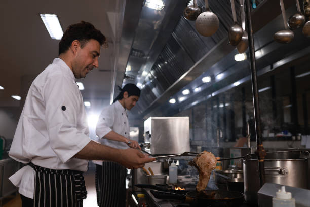 Chef's hands keep wok with fire. Closeup chef hands cook food with fire. Chef man burns food in a professional kitchen. Shot of two cooks preparing food in the kitchen. Cooks prepare meals on the stove in the kitchen of the restaurant or hotel. The fire in the kitchen. las manos del chef mantienen el wok con fuego. las manos del chef de primer plano cocinan la comida con fuego. el chef quema comida en una cocina profesional. toma de dos cocineros preparando comida en la cocina. los cocineros preparan comidas en la estufa