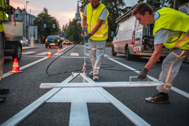 Maintenance Crew Spray Painting A Forward Pointing Arrow Road Sign Maintenance crew spray painting a forward pointing arrow road sign using a spray painter gun and a stencil. They are wearing reflective vests. freshly painted road markings stock pictures, royalty-free photos & images