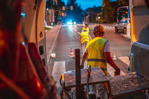 Three construction workers wearing reflective vests preparing a road for spray spray painting. Putting down traffic cones in the night.