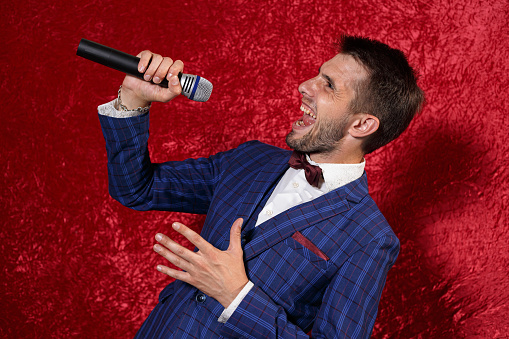 Expressive male emcee in suit performing with microphone in studio on red background