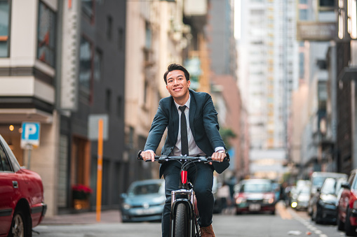 Front view of a smart young Chinese male lawyer commuting in the city with a bicycle. He is smiling and looking away.