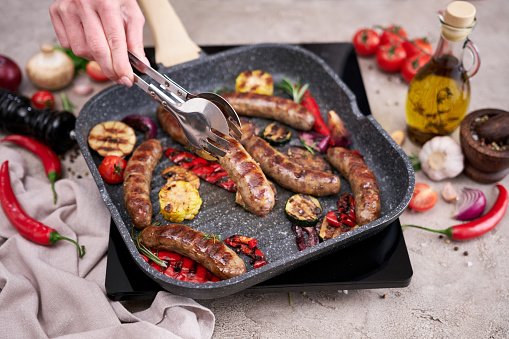 Grilled sausages and vegetables on a grill frying pan on a domestic kitchen.