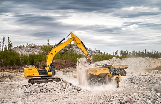 Excavator loading dumpers with blasted stone and causing a cloud of dust in the air
