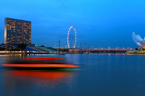 June 3, 2019 - Singapore city, Singapore.\nView of the Singapore city skyline during blue hour with the Ritz-Carlton, Millenia hotel on the left side and the Singapore Flyer with red lights of a moving boat from a long exposure shutter speed.