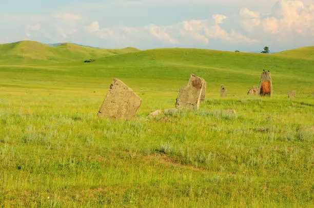 Photo of A group of ancient stone burial stones in a hilly steppe under a clear summer sky.