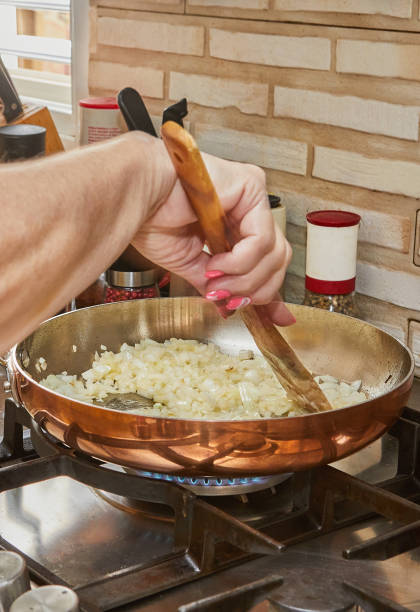 szef kuchni miesza posiekaną cebulę w miedzianym garnku nad ogniem gazowym - copper pans zdjęcia i obrazy z banku zdjęć