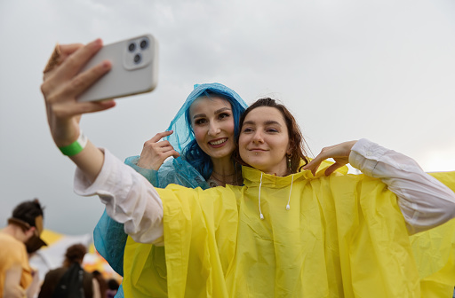 A couple of two young adult LGBT females with tattoos having fun at the summer festival in a rainy day