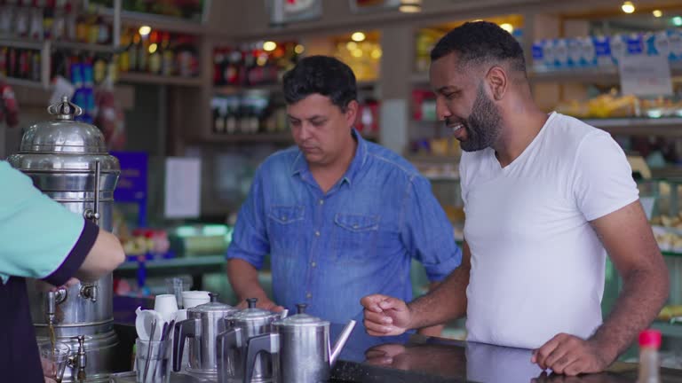 Two Customers ordering coffee standing at cafeteria counter. Candid diverse friends meeting at deli restaurant