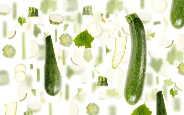 Abstract background made of Zucchini vegetable pieces, slices and leaves isolated on white.