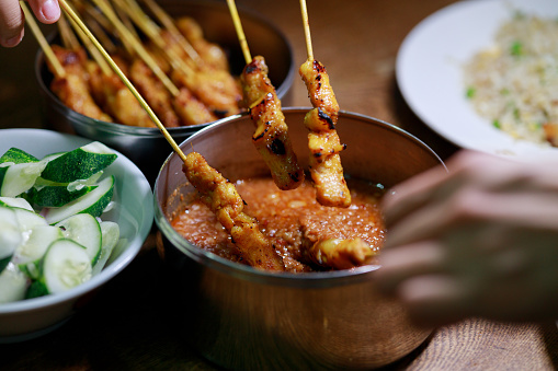 Malaysian food, satay. In a close-up shot, tourists can be seen savoring satay, a mouthwatering Malaysian dish. The satay is paired with a spicy peanut sauce, creating a tantalizing combination of flavors.