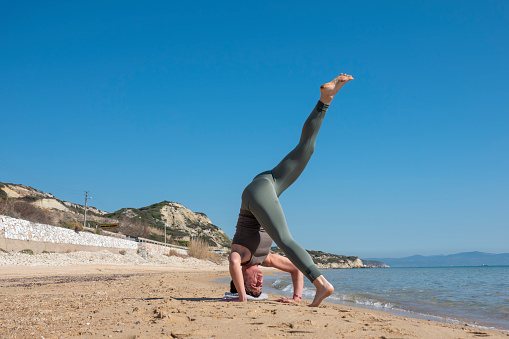 Attractive middle-aged woman practicing yoga on a beautiful beach. A sunny day and a blue sky at an afternoon time.