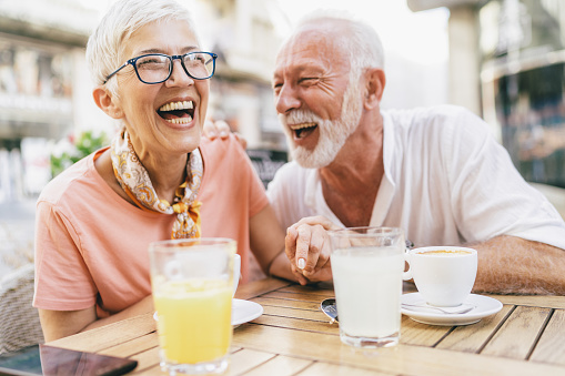 Senior couple sitting in sidewalk cafe drinking coffee and orange juice. Two mature friends talking and laughing together outdoor.