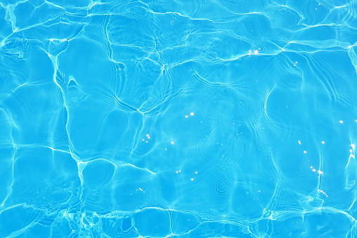 Blue water with ripples on the surface. Defocus blurred transparent blue colored clear calm water surface texture with splashes and bubbles. Water waves with shining pattern texture background.