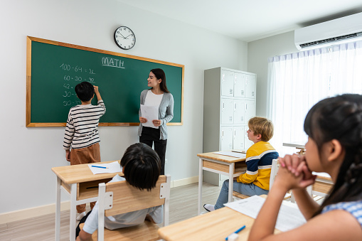 Group of student learn with teacher in classroom at elementary school. Attractive beautiful female instructor master explain and educate young children with happiness and fun activity at kindergarten.