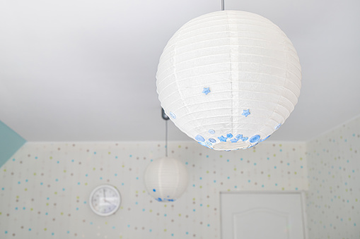 Round white paper lantern lampshade in home room, self decorated with various shape and size buttons.