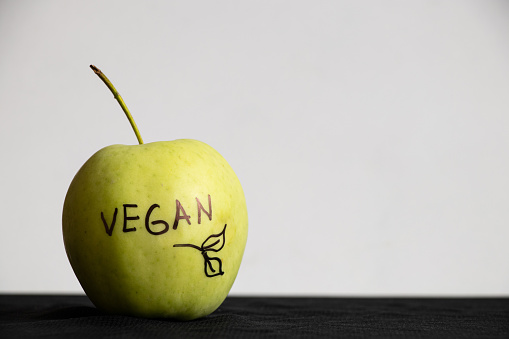Green apple with the inscription vegan on a white background on the table, meat scraps, fruits