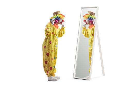 Clown in a yellow costume standing in front of a mirror isolated on white background