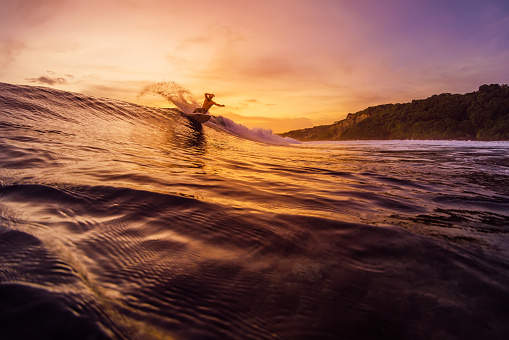 December 14, 2022. Bali, Indonesia. Man in tropical ocean during surfing with sunset or sunrise tones. Surfer ride on wave and make tricks.