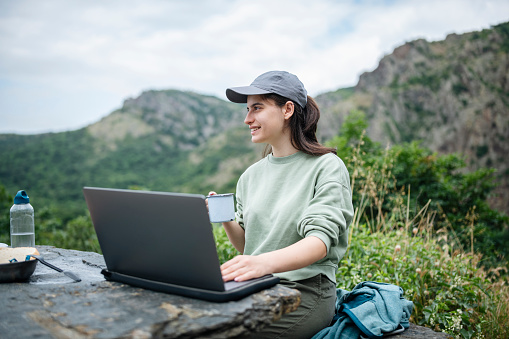 Young woman on picnic in nature using laptop for work.