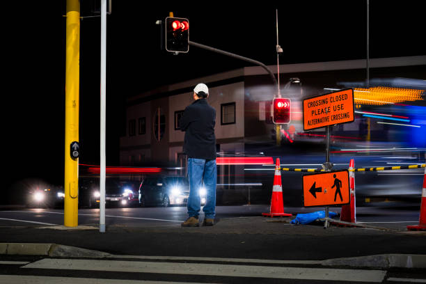 istock Man standing at traffic light. Crossing Closed Please use Alternative Crossing sign at intersection. Bus and car light trails on the road. 1503875126