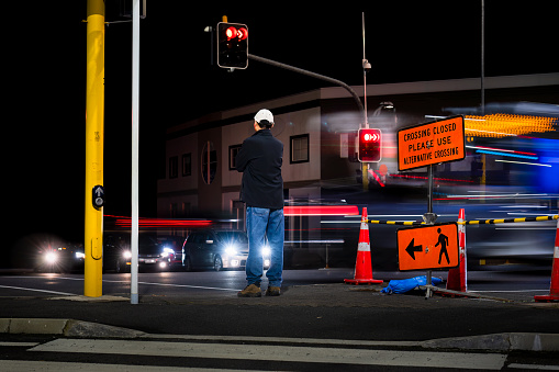 Man standing at traffic light. Crossing Closed Please use Alternative Crossing sign at intersection. Bus and car light trails on the road.