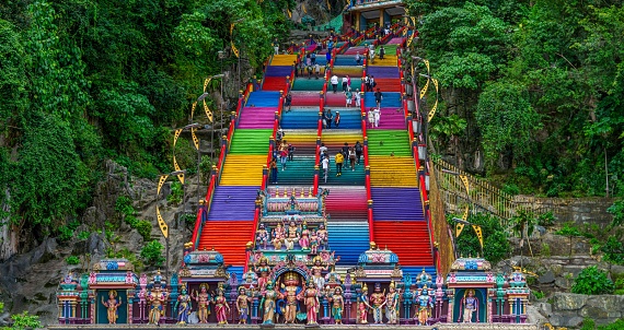 February- 25 -2023-Kuala Lumpur, Malaysia-Visitors and worshipers heading towards Batu cave temple, dedicated to Tamil God Lord Murugan. The stairs are multicolored and circled by monkeys.