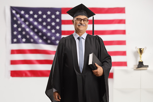 Mature man in a graduation gown holding a book in front of a USA flag