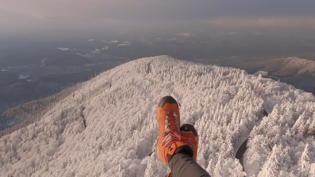 POV paragliding looking down at snowy landscape, with view of feet at the bottom of the frame