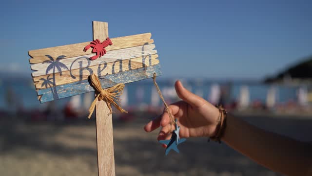 Woman's Hand Playfully Touching Wooden Beach Sign