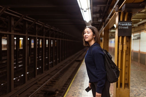 Asian student stands amidst the bustling crowd at a NYC subway station, engrossed in her mobile phone while waiting for her train. Little does she know, the New York City subway system boasts the largest fleet of subway cars in the world, keeping the city moving day and night.
Fun fact: The New York City subway system has over 6,000 subway cars in its fleet, serving millions of commuters each day.