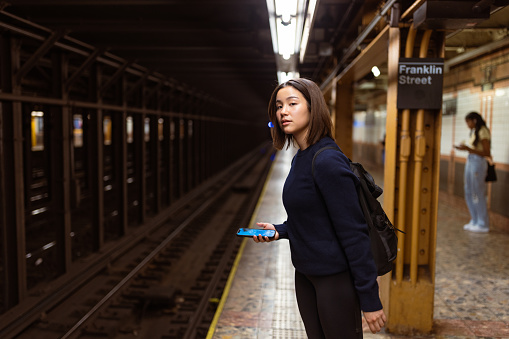 Asian student navigates the NYC subway system using her mobile phone, ensuring a seamless commute. The vast network of subway lines in the city spans over 800 miles, connecting neighborhoods and boroughs with efficiency and convenience.
Fun fact: The New York City subway system is one of the largest in the world and covers a vast network of tracks, allowing commuters to travel throughout the city quickly and conveniently.