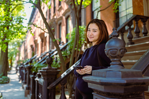Asian student discovers tranquility as she sits on a characteristic doorway, immersing herself in the neighborhood's timeless charm. 
Fun fact: The West Village is home to some of the city's most delightful restaurants and cafes, offering a wide range of culinary delights for residents and visitors alike