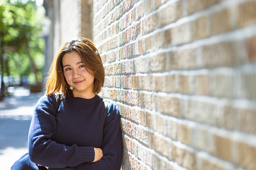 With the iconic red brick buildings of the West Village as a backdrop, a cute Asian student confidently looks into the camera, showcasing her bright smile.

Fun fact: The West Village is dotted with beautiful and historic trees, adding a touch of natural beauty to the neighborhood's character.