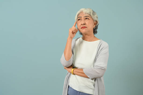 Confused and thoughtful senior woman thinking and looking up expressing doubt and wonder isolated blue background. stock photo