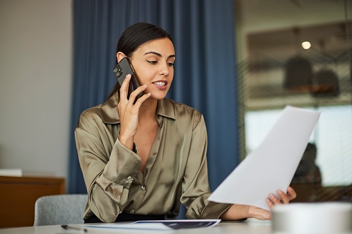 In this stock photo, a young businesswoman multitasks effectively as she makes a phone call while reviewing a document