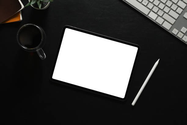 istock Digital tablet with white empty display, stylus pen, coffee cup and keyboard on black leather. 1503914122