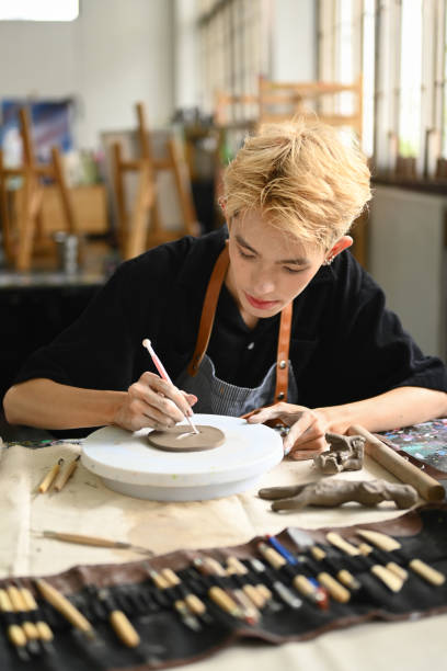 istock Focused man pottery artist decorating clay plate on table at ceramic workshop. Indoors lifestyle activity and hobbies concept. 1503914131