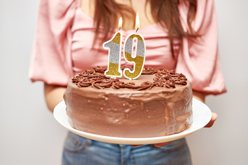 The girl is holding a festive cake with a candle in the form of the number 19. The concept of a birthday celebration.