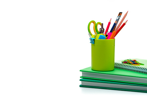 Multicolored school or office supplies in a desk organizer and green books isolated on white background. The composition is at theright of an horizontal frame leaving useful copy space for text and/or logo at the left. High resolution 42Mp studio digital capture taken with Sony A7rII and Sony FE 90mm f2.8 macro G OSS lens