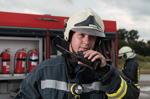 Fireman using walkie talkie at rescue action fire truck and fireman's team in background.
