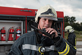 Fireman using walkie talkie at rescue action fire truck and fireman's team in background